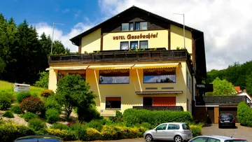 Hotelgebäude mit Autos, Bäumen und Wolkenhimmel.