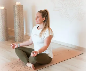 Frau meditiert auf Yogamatte im Raum.