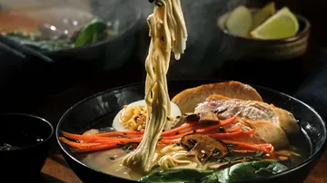 Hand hebt Nudeln aus Ramen-Schüssel mit Gemüse.