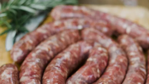 Raw sausages on wooden board with herbs.