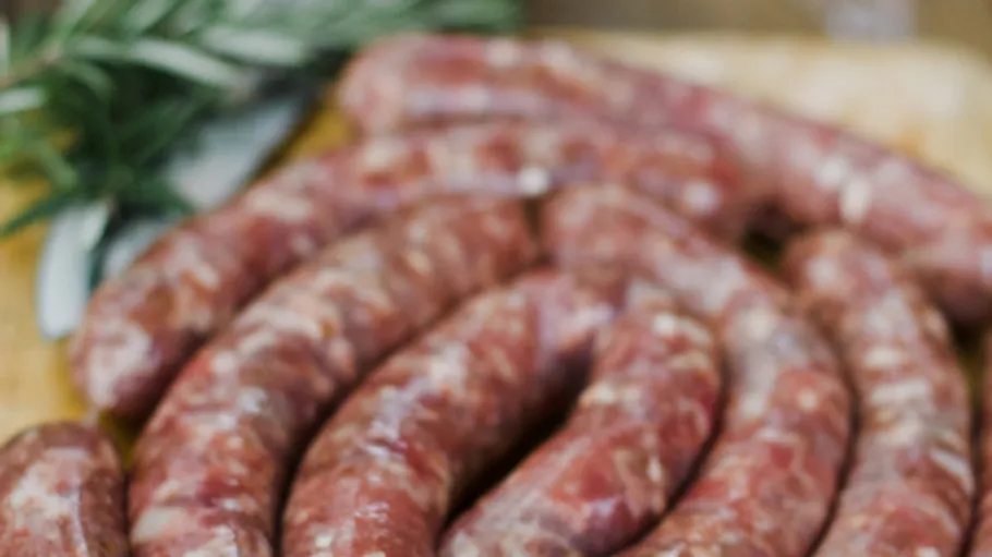 Raw sausages on wooden board with herbs.