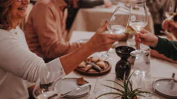 Zwei Personen stoßen mit Weingläsern beim Abendessen an.