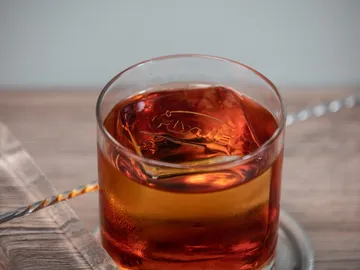 A glass of brown drink stands on a surface.