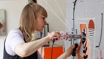 Woman using tufting gun on textile art.