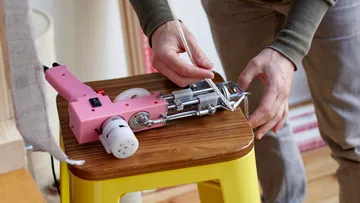 Person handling yarn tool on wooden stool.