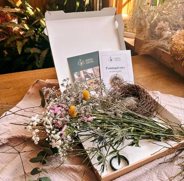 Box mit Blumen und Kranzmaterialien, sonniger Raum.