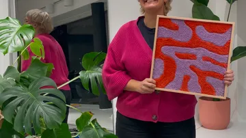 Person hält bunte Textilkunst neben Pflanzen.