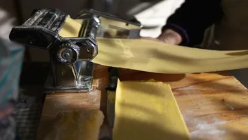 Nudelmaschine rollt Teig auf Holzfläche.