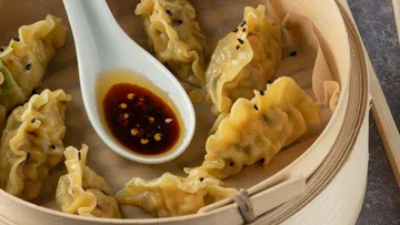 Dumplings in bamboo steamer with dipping sauce.
