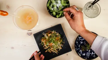 Person eating salad and edamame on wooden table.