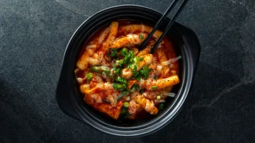 Spicy Korean rice cakes in black bowl.