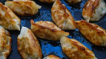 Fried dumplings on a dark cooking surface.