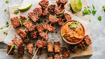 Tempeh-Spieße mit Sauce auf Holzbrett.