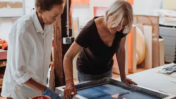 Zwei Frauen arbeiten drinnen an einem Druckprojekt.