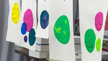 Colorful circle prints drying on rack.