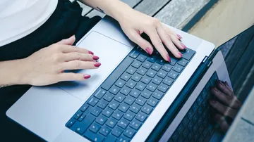 Hände tippen auf Laptop im Freien auf Holz.
