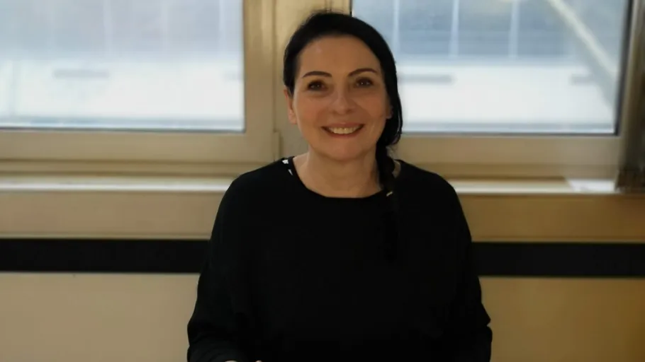 Smiling person standing indoors near a window.