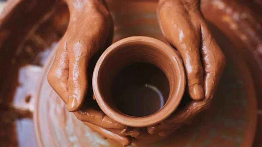 Hands shaping clay pot on pottery wheel.