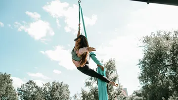 Woman performing aerial silk outdoors, blue sky.