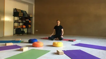 Person meditating in yoga studio with cushions.