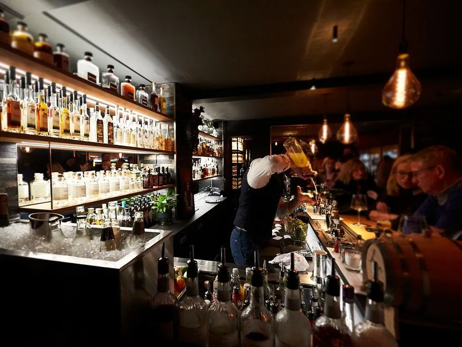 Bartender mixt Getränke an einer beleuchteten Bar.