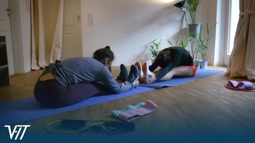Two people stretching indoors on yoga mats.