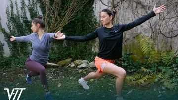 Two women doing yoga outdoors with greenery.