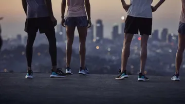 Runners standing on hill, city skyline background.