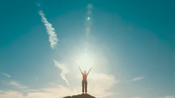 Person stands with arms raised atop a hill.