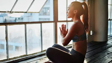Woman meditating by large window, sunlight streaming.