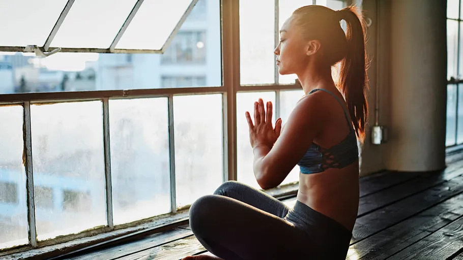 Woman meditating by large window, sunlight streaming.