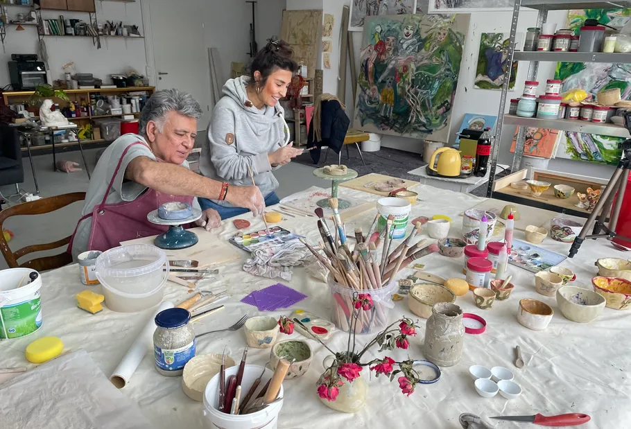 Two people painting at a cluttered art studio.