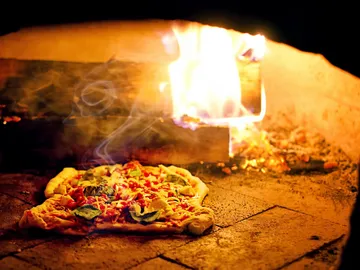 Pizza is lying on the stone while flames burn.