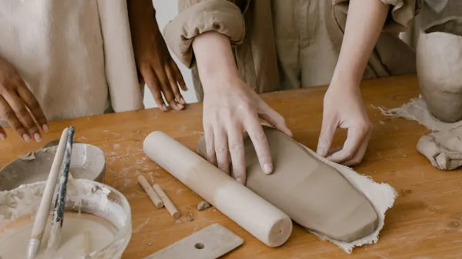 Hands shaping clay on a wooden table.