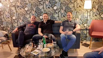 Drei Männer sitzen auf Sofa, lächelnd, Wohnzimmer.
