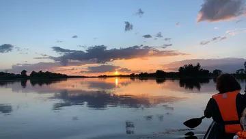 Person canoeing on calm lake at sunset.