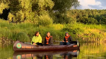 Three people canoeing on a calm river.