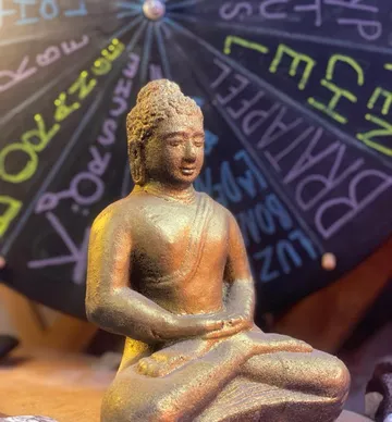 Bronzene Buddha-Statue vor einer Tafel.