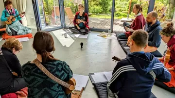 Menschen spielen Instrumente im Kreis drinnen.