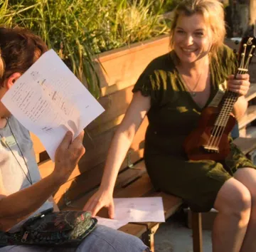 Woman with ukulele smiling, sitting on a bench.