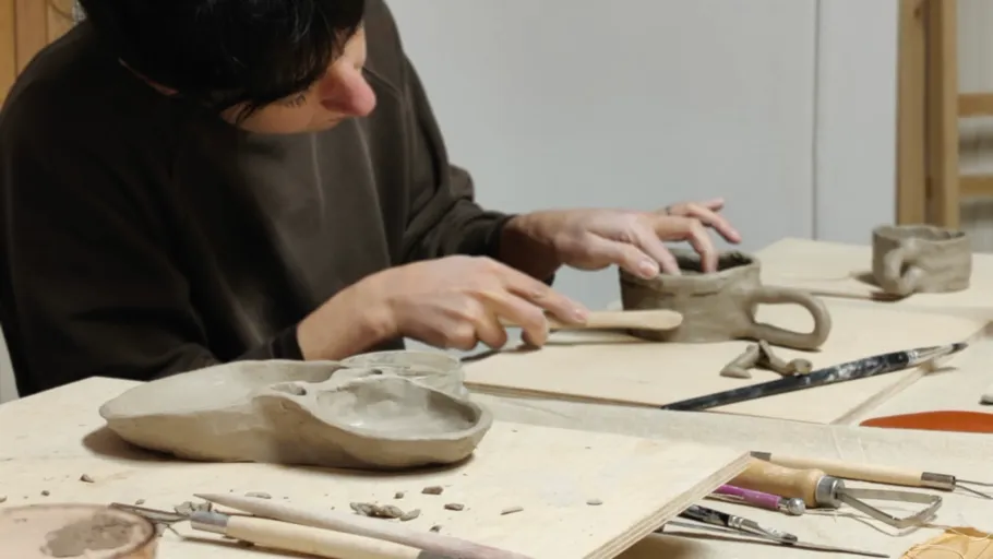 Person sculpting clay in a workshop setting.