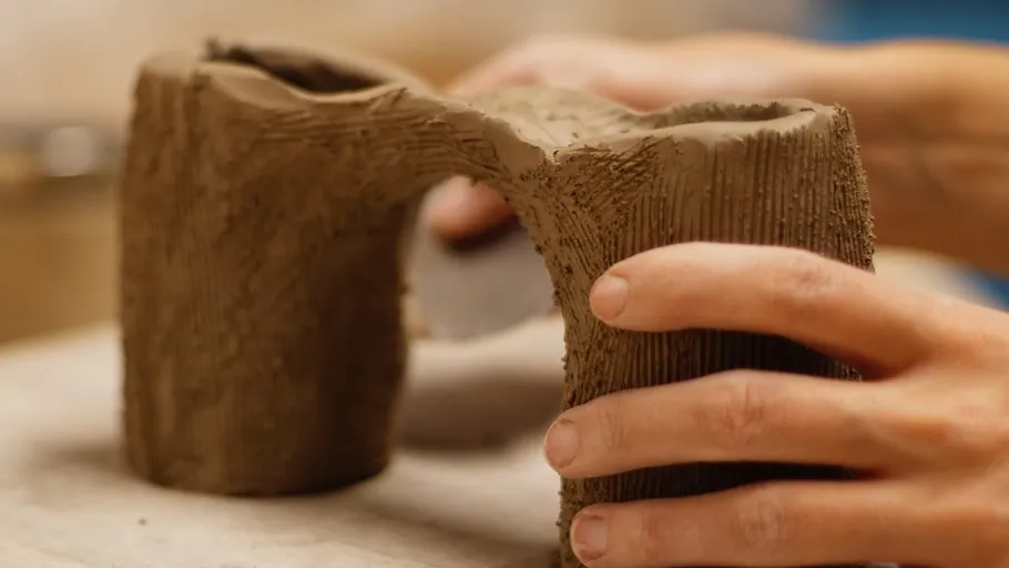 Hands shaping a clay object on table.