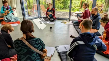 People playing instruments in a circle indoors.