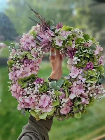Floral wreath held in sunny garden.