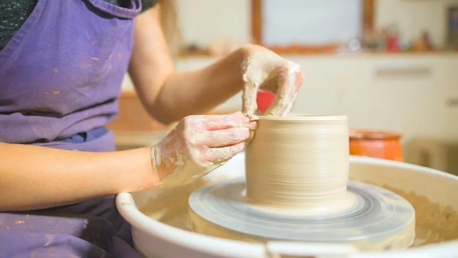 Person shaping clay on a pottery wheel indoors.
