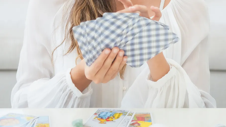 Person holding tarot cards on a table.