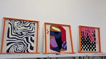 Drei gerahmte abstrakte Wandteppiche auf Ausstellungstisch.