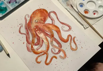 Octopus watercolor painting, palette and brushes nearby.