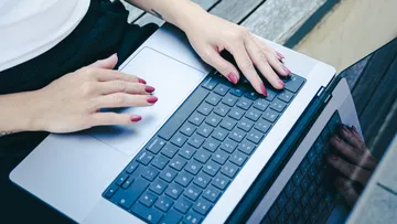 Hände tippen auf Laptop, Außentisch.