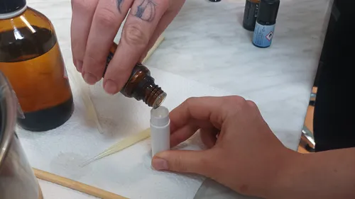 Hands pouring liquid into small container on table.